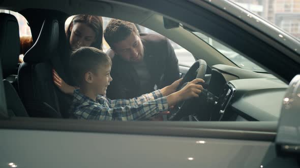 Family with Son Purchasing Car in Showroom, Kid Having Fun with Steering Wheel alt