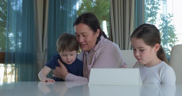 Grandma Entertaining Her Little Grandchildren with a Tablet Computer Game