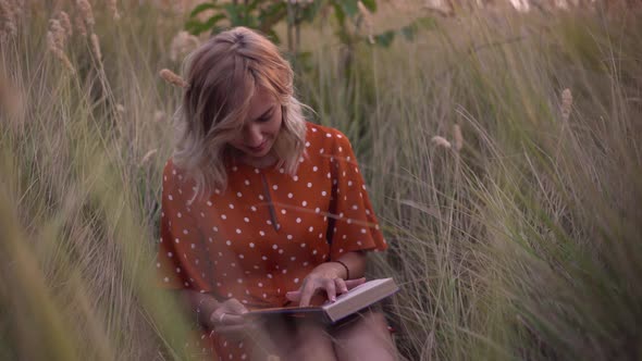Beautiful Happy Young Woman in Field of Spikelets and Wheat with Book on the Sunset Blonde in the alt