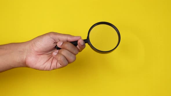 Hand Holding Magnifying Glass Against Yellow Background alt