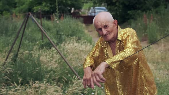 Old Bald Man in Yellow Festival Shirt Looks Among Grass