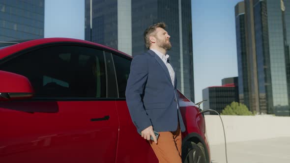Smart Businessman with Smart Phone Waiting Electric Vehicle Charging Battery alt
