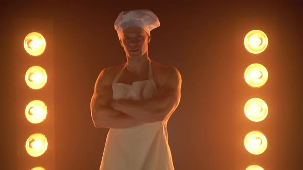 Portrait of Muscular Chef Wearing White Apron and Chef Hat on Smoky Background alt