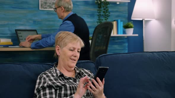 Pleasant Senior Older Lady Resting on Couch Using Applications on Smartphone alt