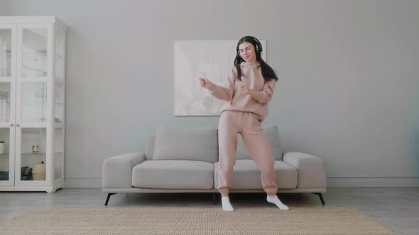 Millennial girl wearing headphones happily dancing jumping alone listening music