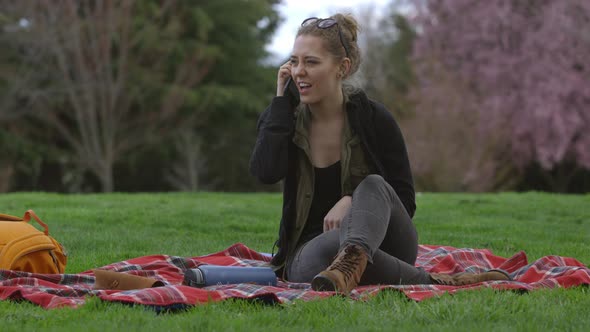Young woman at park sitting on blanket talking on cell phone