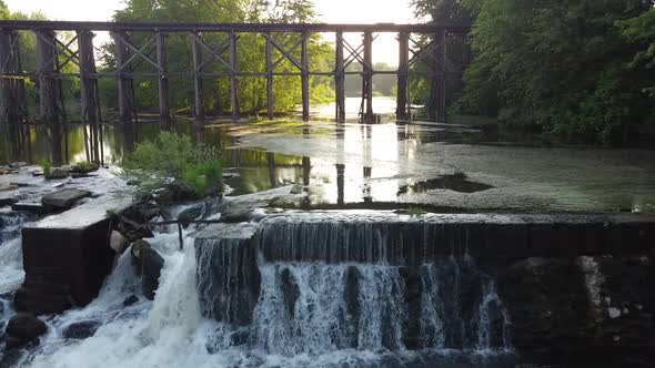 Aerial Pan Over Dam with Waterfalls and Old Railroad Bridge in Background