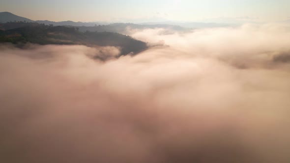 4K aerial view over mountain at sunrise in heavy fog. golden morning sunlight alt