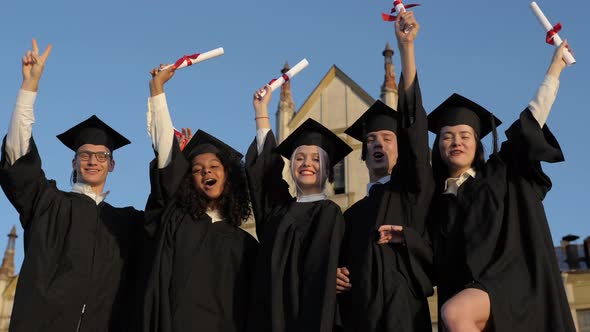 Happy Group of Students with Arms Up at Their Graduation. alt
