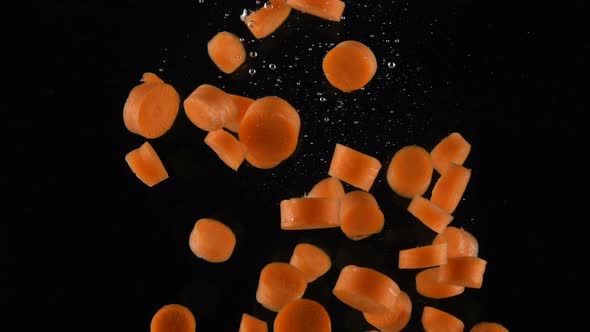 Chopped Carrot Falls in Water on Black Background
