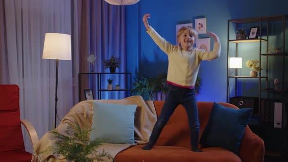 Happy Child Girl Kid Dancing Trendy Dance While Listening to Music at Home Alone Standing on Sofa alt