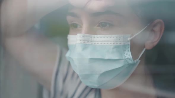 The girl in the mask stands at the window alt