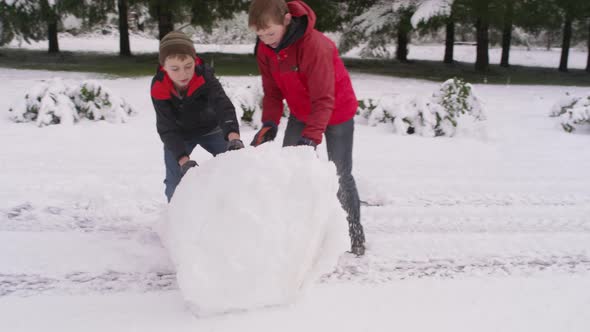 Two boys rolling a snow ball in winter