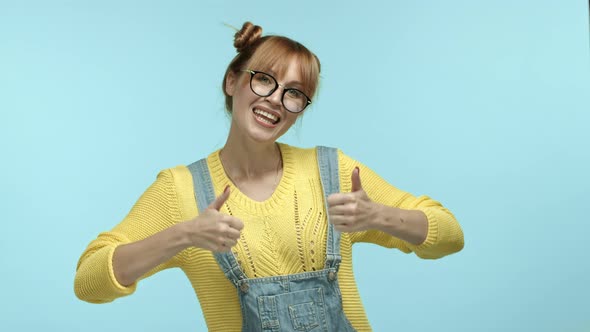 Funny Hipster Girl in Glasses and Overalls Showing Thumbsup Gesture Saying Yes and Dancing Happy