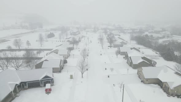 Drone view over rural residential neighborhood with snow falling with cloudy sky.