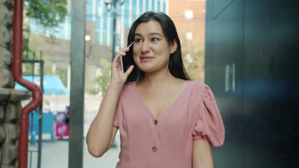 Dolly Shot of Beautiful Asian Woman Walking Outdoors Speaking on Mobile Phone and Smiling Outdoors alt