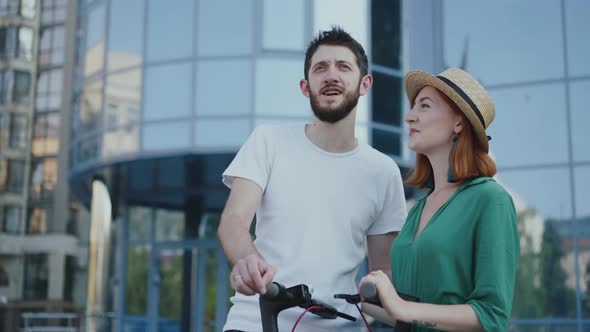 Couple in Love Stands at Scooters Man Talking and Girl Looking and Smiling alt