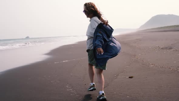 Young Woman Runs on a Black Volcanic Beach Along the Ocean alt