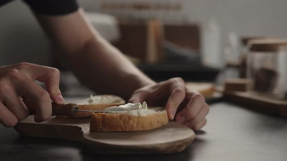 Slow Motion Man Spread Cream Cheese Over Ciabatta Slice on Olive Board alt