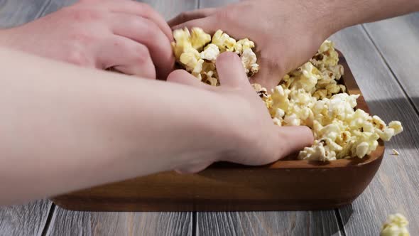 A Company of Three Friends Simultaneously Takes Ready Popcorn from A Wooden Plate