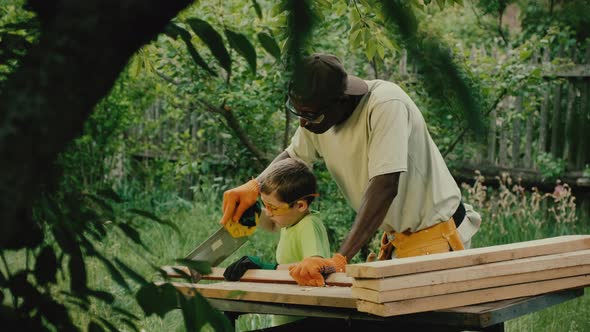 African American Carpenter Helps White Boy Cut Wooden Plank