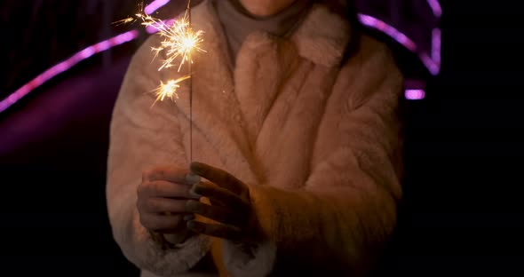 Sparklers in Young Woman Hands. Sparks Scatters in Different Directions at Neon Lights Background alt