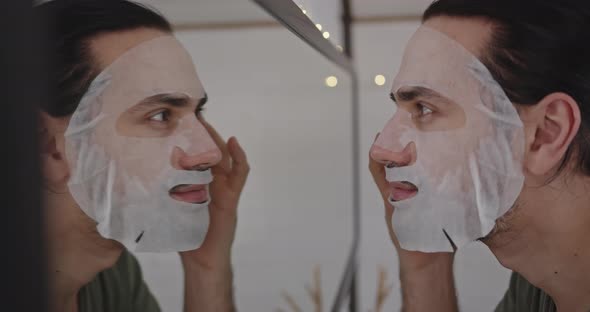 Closeup of a Young Man Face in Front of a Mirror Wearing a Cosmetic Sheet Mask