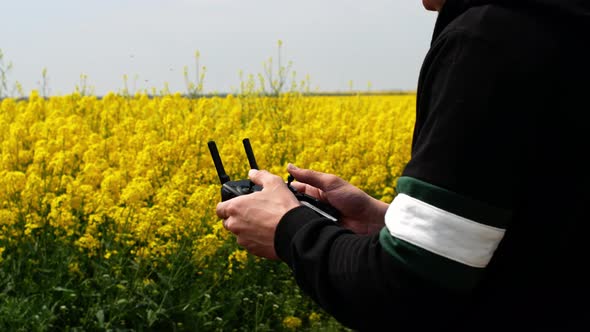 Close-up shot of drone remote control in men's hands. A man flying on a drone over a yellow field alt