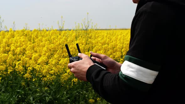 Close-up shot of drone remote control in men's hands. A man flying on a drone over a yellow field