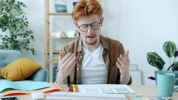 Young Man Designer Making Online Video Call with Computer Camera Talking and Showing Smartphone alt