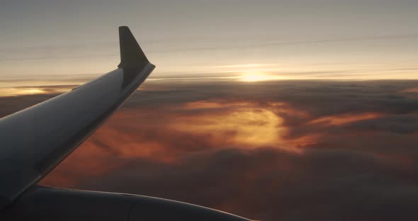 Wing of an Airplane Flying Above the Clouds with Sunset Sky. View From the Window of the Plane. alt