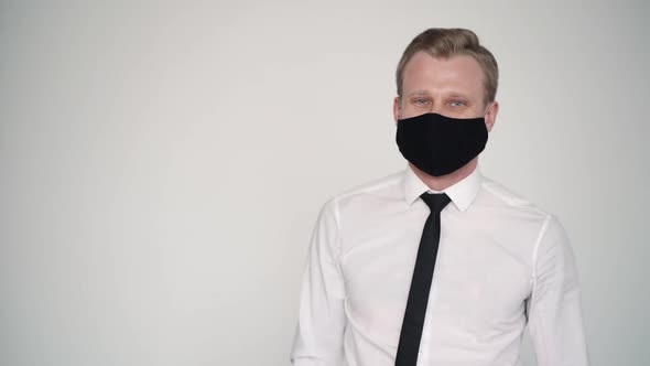 Portrait of Business Male Wear Facial Mask Turning To Look at Camera. Man on White Wall Background.