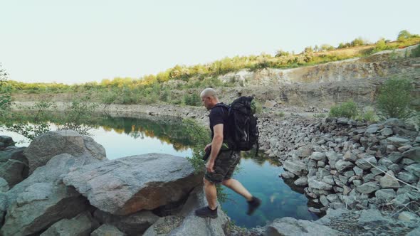 A tourist in summer clothes walks on the edge of a quarry with huge stones alt