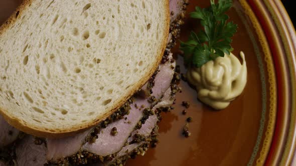 Rotating shot of delicious, premium pastrami sandwich next to a dollop of dijon mustard  alt