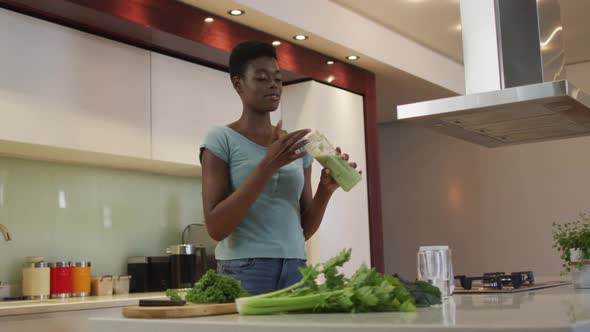 Smiling african american attractive woman tasting homemade smoothie in kitchen alt
