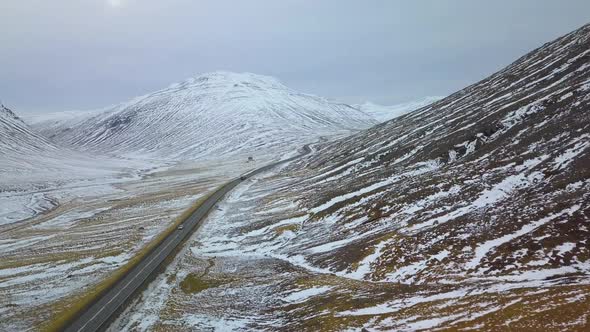 Aerial view of vehicles driving down highway in between snowy mountains alt