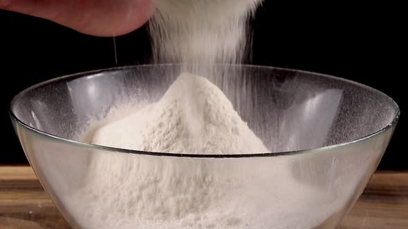Sifting flour through a sieve into a glass bowl in the kitchen. alt