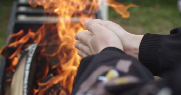 Close Up Faceless Person Holding Hands By Fire Burning in Charcoal Grill Outdoors Green Grass