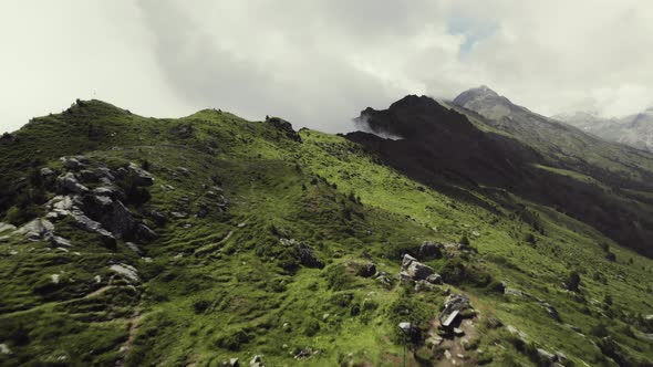 Aerial drone shot of a grass covered mountain top with a small trail leading along with a person hik alt