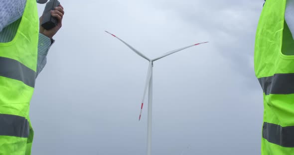 Engineers shake hands against wind turbine generating electricity on windmill.