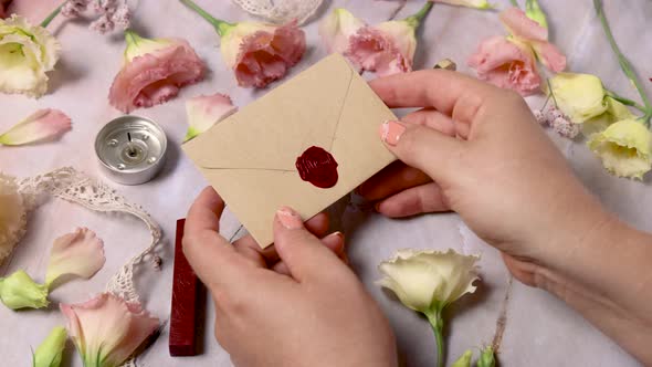 Hands taking wax sealed envelope from a marble table near pink flowers alt