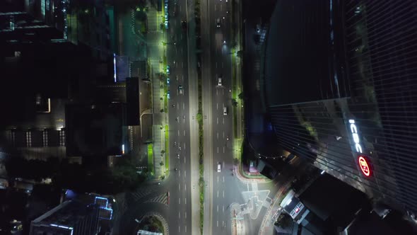Aerial Birds Eye Overhead Top Down View of City Traffic at Night Next To Skyscraper Tower Building alt