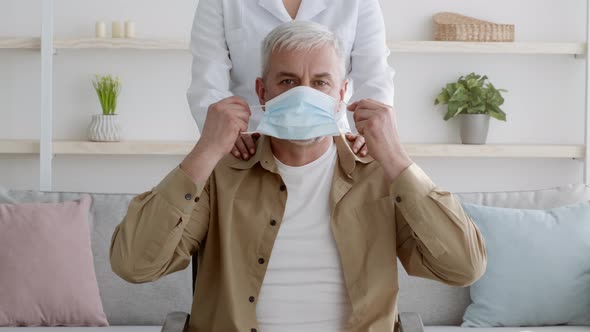 }Disabled Man In Wheelchair Putting On Face Mask At Home alt