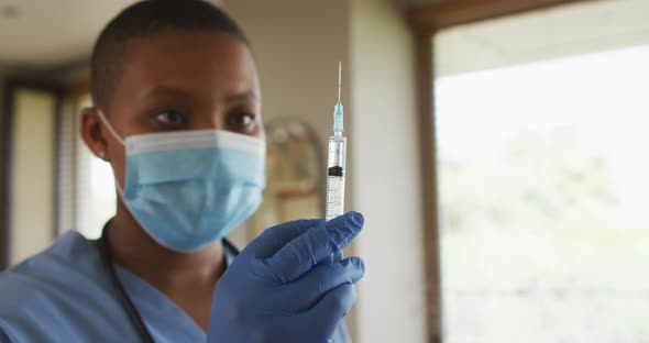 African american female doctor wearing face mask preparing covid vaccine for patient alt