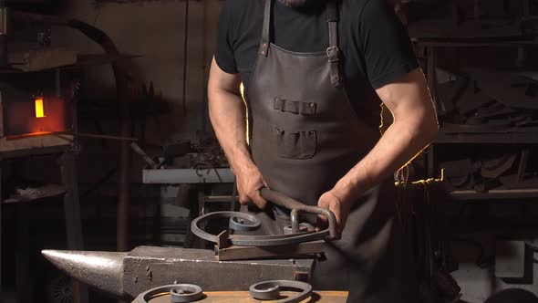 Man Works with Metal in a Workshop. The Smith Makes an Element of Decor