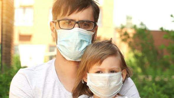 Father with Little Girl Look at Camera in Medical Masks on Background of Summer Park on Sunset