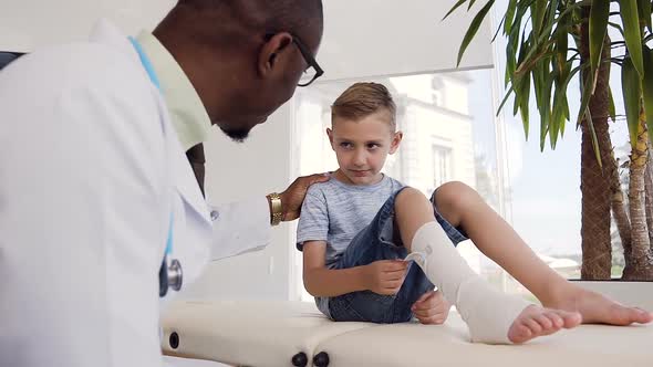 African Doctor Talking with Little Patient with Bandage on the Leg alt