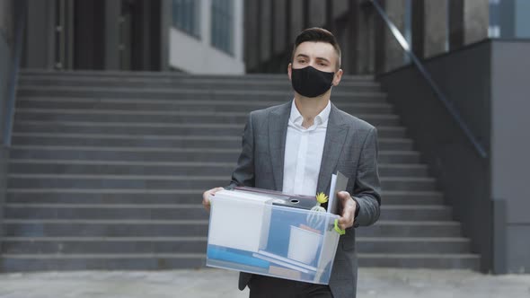 Fired Sad Young Businessman in Medical Mask Carries Box With Personal Belongings Leaving the Office