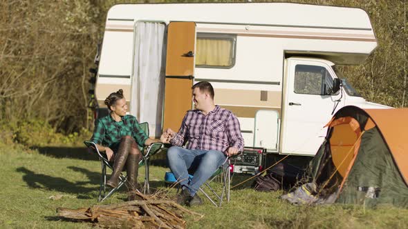 Hipster Couple Sitting on Their Camping Seats and Holding Hands alt