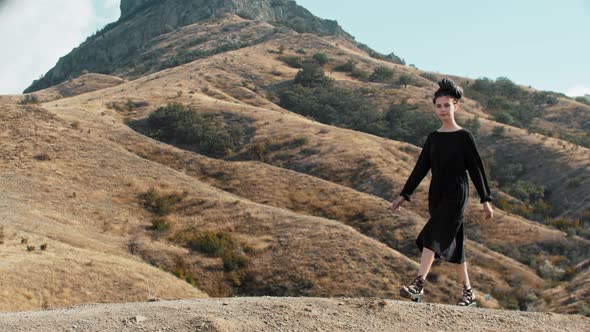 Young Woman in Summer Dress Walking on the Mountains  Looks in the Camera and Waving with Her Hand alt